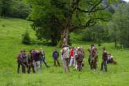Gruppe von Jägern und Interessierten diskutieren auf einer Weide vor altem Baum. 