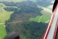 Blick aus einem kleinen Flugzeug auf Wald und Felder.