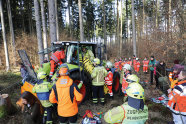 Feuerwehr und Sanitäter stehen im Wald um einen Traktor und versuchen einen Menschen aus der Maschine zu befreien