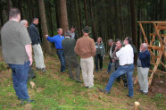 Eine Gruppe mehrerer Männer diskutiert im Wald bei einem Drückjagdbock.