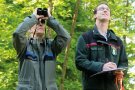 Zwei Personen mit Blick nach oben mit Fernglas und Klemmbrett in der Hand.