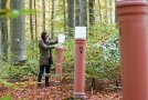 Person liest Werte an einem orangen Messrohr im Boden ab.