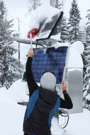 Mann schaufelt Schnee von einem Solarpanel.