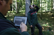 Zwei Menschen stehen mit Tablett und Fernglas im Wald und nehmen Daten auf.