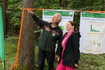 Ein Mann und eine Frau stehen im Wald. Der Mann zeigt nach oben
