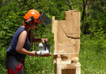 Frau in Waldarbeitermontur mit Motorsäge an Holzstamm