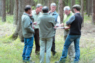 Sechs Männer stehen im Kreis im Wald