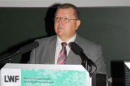 Das Bild zeigt einen Mann im grauen Anzug, der hinter einem Rednerpult steht und spricht.