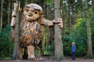 Eine riesige Trollskulptur aus Holz steht in einem Wald