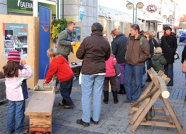 Das Bild zeigt eine Gruppe Kinder und Erwachsener in einer Einkaufsstraße. Im Hintergrund befindet sich ein forstlicher Informationsstand.