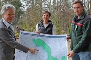 Drei Personen zeigen auf eine Karte die den Nationalpark Bayerischer Wald zeigt.