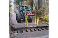 Traktor hebt mit der Frontgabel das Gitter eines Durchlasses hoch.