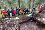 Personengruppe steht um ein rechteckiges Loch im Boden und verfolgt einen Vortrag.