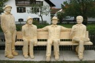 Vier lebensgroße Holzmänner sitzen auf einer Bank