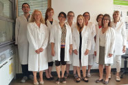 Eine Gruppe, bestehend aus neun Frauen und einem Mann, alle in Laborkittel gekleidet, lächeln in die Kamera