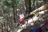 Ein Mitarbeiter der Waldinventur steht mit Ausrüstung im Nadelwald an einem Steilhang
