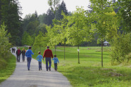  Einige Erwachsene und Kinder gehen auf einem Weg am Waldrand spazieren.