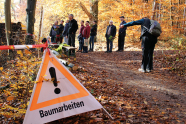 Ein Herbsttag. Ein Waldweg, im Vordergrund ein Achtungsschild mit Aufschrift "Baumarbeiten", im Hintergrund Menschen