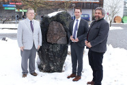 Drei Männer stehe vor einem Stein im Schnee