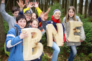 Gruppe Kinder, die die Buchstanben B, N und E aus Holz hochhalten.