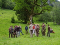 Menschengruppe diskutiert auf einer Wiese vor einem sehr alten Baum.